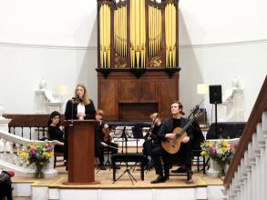 Professor Laura Tunbridge delivering lecture, with student musician on stage behind
